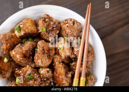 Plaque blanche avec des morceaux de poulet dans un style asiatique avec des baguettes. Vue d'en haut. Poulet chinois sauce aigre-douce. Banque D'Images
