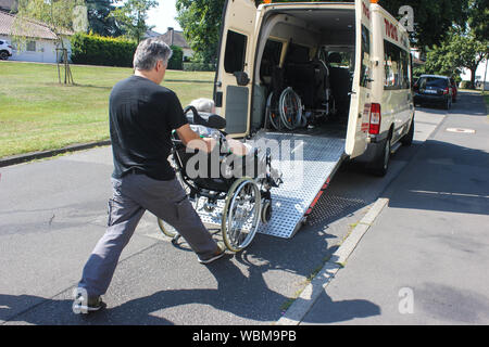 Soignant poussant une ancienne dame âgée en fauteuil roulant sur une rampe vers un van de transport médical spécialisé par une journée ensoleillée pour une personne handicapée. Banque D'Images
