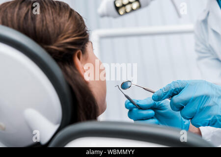 Portrait de dentiste dans des gants en latex bleu holding instruments dentaires près de femme Banque D'Images