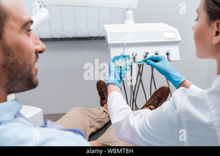 Portrait de dentiste holding toothbrush près de modèle de dents et l'homme en clinique Banque D'Images