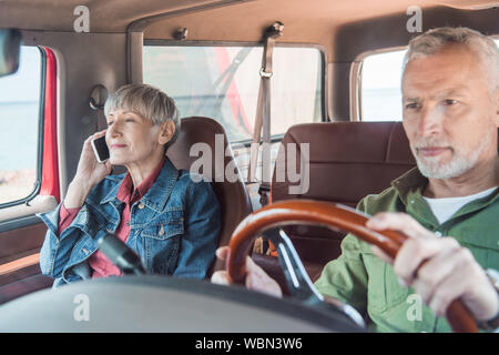 Senior Woman talking on smartphone pendant que mari driving car Banque D'Images