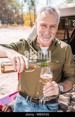 Smiling senior homme debout près de voiture et de verser le vin dans le verre de vin Banque D'Images