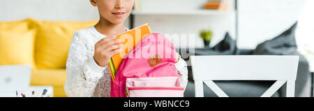 Vue panoramique tourné de Happy Child holding book près de sac à dos à la maison rose Banque D'Images
