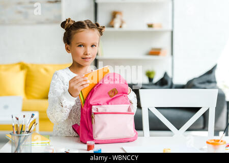 Happy Child holding book près de sac à dos à la maison rose Banque D'Images