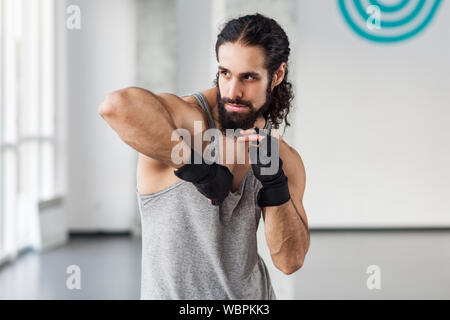 Portrait de jeune homme musclé en colère adultes avec les cheveux bouclés et la préparation de commandes de lutter avec le coude en noir gants, montrant le kickboxing professionnel Banque D'Images