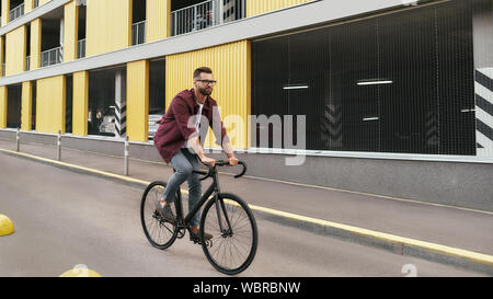 Vélo partout. Vue latérale du bel homme avec chaume dans les tenues de rouler sur son vélo le long d'une route contre bâtiment jaune. L'activité de fin de semaine. Cycle de vie. Bannière web Banque D'Images