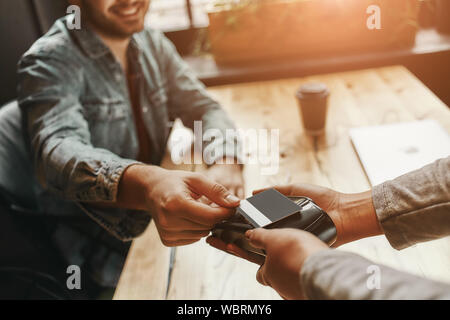 Main de client de payer par carte de crédit sans contact avec la technologie NFC. Garçon avec un lecteur de carte de crédit provenant de la machine à une possession d'une carte de crédit. Se concentrer sur les mains. Plan horizontal Banque D'Images