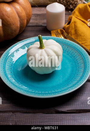 Citrouille blanc sur plaque bleue avec serviette sur fond en bois avec des bougies et orange citrouille. Notion d'action de grâce et l'Halloween set de table Banque D'Images