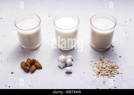 Trois autres noix de coco lait végétalien, d'avoine et d'amande dans les verres suivant pour les ingrédients sur un fond gris Banque D'Images