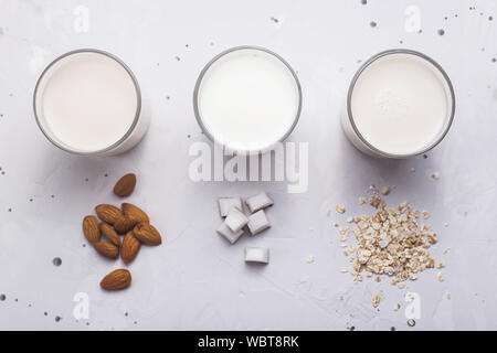 Trois autres noix de coco lait végétalien, d'avoine et d'amande dans les verres suivant pour les ingrédients sur un fond gris. Haut de la vue, télévision lay Banque D'Images