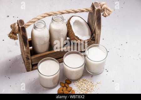 Trois autres noix de coco lait végétalien, d'avoine et d'amande dans les verres suivant pour les ingrédients et une boîte en bois avec des bouteilles de lait sur une table gris Banque D'Images