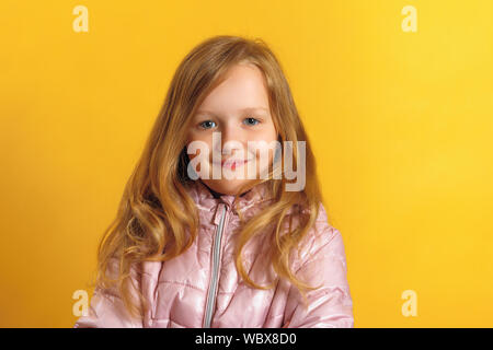 Portrait of a cute little girl dans une veste sur un fond jaune. Concept d'automne et d'hiver. Banque D'Images