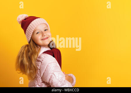 Portrait of a cute little girl dans une veste, écharpe et chapeau sur un fond jaune. L'hiver et l'automne concept. Banque D'Images