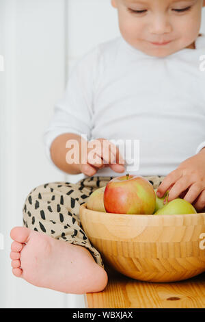 Lly blond bébé garçon est explore, joue avec des pommes de backet. Banque D'Images