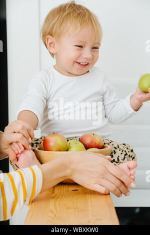 Lly blond bébé garçon est explore, joue avec des pommes de backet. Banque D'Images