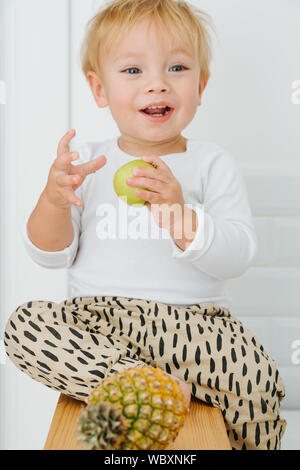 Lly blond bébé garçon est explore, joue avec des pommes de backet. Banque D'Images