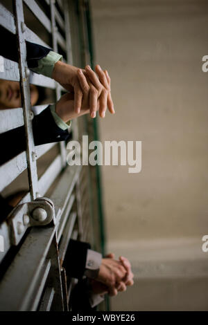 Les mains d'un jeune homme d'adultes et d'un collègue à travers les barreaux d'une cellule de prison dans un bâtiment abandonné. Banque D'Images