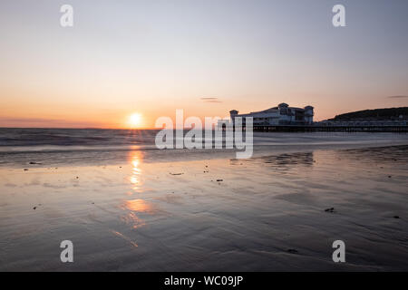 Le Grand Pier à Weston-super-Mare au coucher du soleil avec la lumière se reflétant sur la plage de sable. Juillet 2019 Banque D'Images