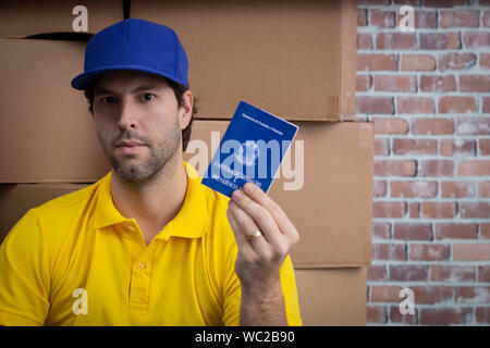 Mailman brésilien tenant son carnet de travail sécurité sociale brésilienne document, dans un dépôt avec un beaucoup de boîtes. Banque D'Images