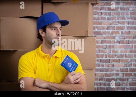 Mailman brésilien tenant son carnet de travail sécurité sociale brésilienne document, dans un dépôt avec un beaucoup de boîtes. Banque D'Images