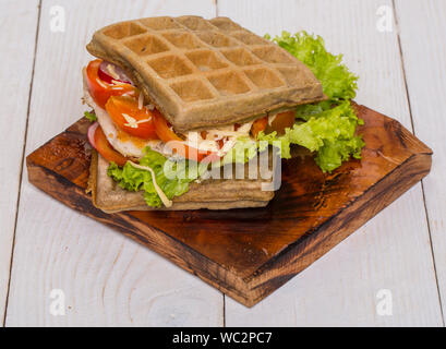 Sandwich gaufres avec du poulet, légumes et fromage sur fond de bois Banque D'Images