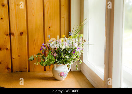 Style Vintage flower bouquet fait de fleurs sauvages trouvés en forêt et prairie, debout dans le vieux pot de crème sur le rebord de fenêtre, l'été dans la maison de grand maman con Banque D'Images