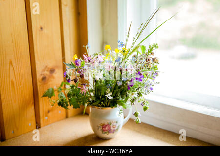 Style Vintage flower bouquet fait de fleurs sauvages trouvés en forêt et prairie, debout dans le vieux pot de crème sur le rebord de fenêtre, l'été dans la maison de grand maman con Banque D'Images