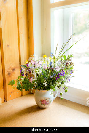 Style Vintage flower bouquet fait de fleurs sauvages trouvés en forêt et prairie, debout dans le vieux pot de crème sur le rebord de fenêtre, l'été dans la maison de grand maman con Banque D'Images