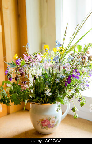 Style Vintage flower bouquet fait de fleurs sauvages trouvés en forêt et prairie, debout dans le vieux pot de crème sur le rebord de fenêtre, l'été dans la maison de grand maman con Banque D'Images