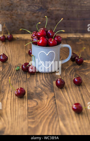 Cerises fraîches en gris tasse en forme de coeur sur table en bois, teinté Banque D'Images