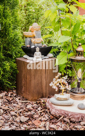 Petit jardin privé accueil fontaine avec statue de Bouddha méditant entre les arbres et arbustes. Jardin zen' concept. Banque D'Images