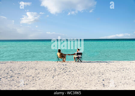 Plage de l'océan comme un couple assis sur des chaises près du bord de l'eau. Montagnes retirées. Banque D'Images