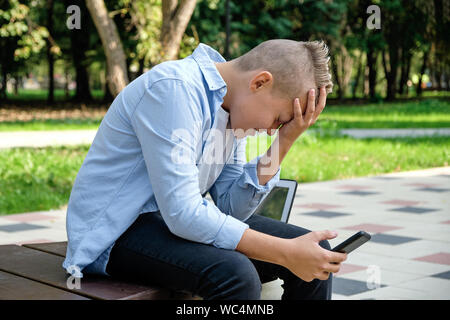 Problèmes d'enfants. moderne Jeune homme dans le parc avec le téléphone en colère. La dépression est un trouble mental dû à des réseaux sociaux. La vie en ligne, depressi Banque D'Images