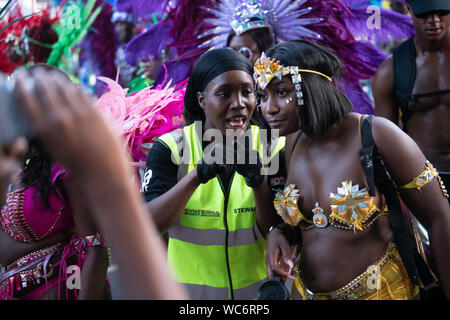 Synterna Administrateur sécurité parler à la Carnival effectuées au carnaval de Notting Hill. D'autres artistes interprètes ou exécutants dans l'arrière-plan Banque D'Images