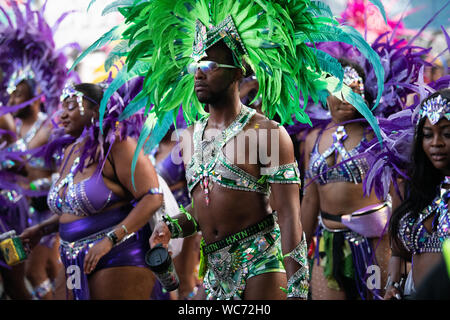 Danseur portant des plumes et à la recherche dans l'appareil photo au carnaval de Notting Hill à Londres. D'autres danseurs dans l'arrière-plan Banque D'Images