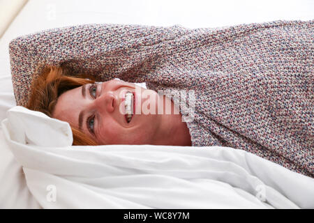 Une belle femme établit dans son lit, souriant alors que se réveiller le matin Banque D'Images