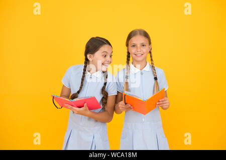 La lecture et l'interprétation. Les petits enfants holding books fond jaune. Intérêt sincère. Peu de filles avec des livres pour enfants ou de l'encyclopédie. Bibliothèque de l'école. Des livres éducatifs pour l'école. La lecture de livres. Banque D'Images