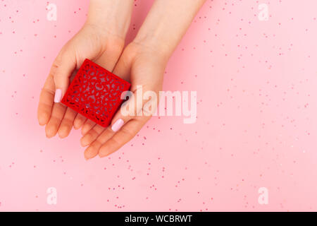 La fille tient dans ses mains une boîte à motifs rouge avec un anneau. Vue de dessus sur un fond rose avec place pour le texte. Glitter en arrière-plan. Banque D'Images