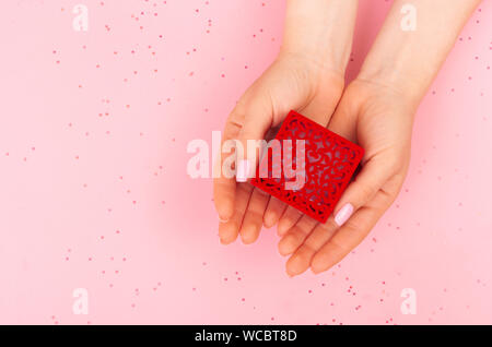 La jeune fille tient à deux mains une boîte en velours rouge avec un anneau. Vue de dessus sur un fond rose avec place pour le texte. Scintille sur l'arrière-plan. Banque D'Images