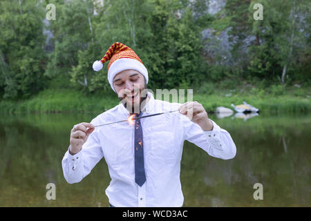 L'homme joyeux dans un costume, cravate et nouvelle année ou santa hat détient un sparkler. Nouvelle ans parti de l'entreprise Banque D'Images