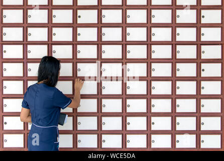 Une jeune femme ouvre boîte aux lettres sur mur plein de boîtes aux lettres. Femme à l'aide de boîtes de dépôt sur le mur. Banque D'Images