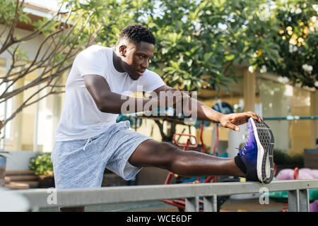 Monter African American man standing avec jambe levée sur rambarde métallique faisant l'exercice d'étirement lors de l'entraînement dans la région de park Banque D'Images