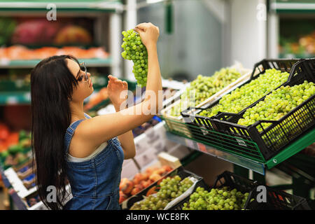 L'acheteur choisit de raisins dans le magasin. Fille envisage d'aliments dans le marché. L'homme achète des fruits sains Banque D'Images