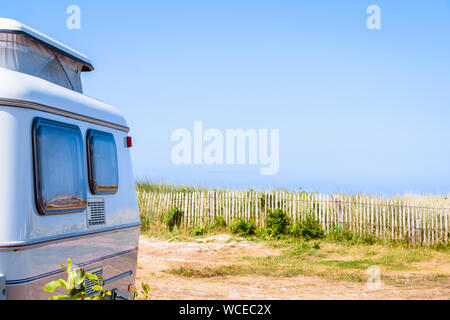 Une petite caravane avec pop-up garé sur le toit avec vue mer sur un terrain de camping délimité par une clôture en bois. Banque D'Images