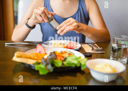 Meulage femme poivre oeufs frits au petit déjeuner avec un verre d'eau sur la table. Banque D'Images