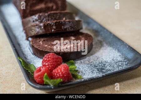 Swiss roll avec de la confiture au chocolat décoré avec des framboises dans une assiette. Des bonbons. Focus sélectif. Banque D'Images