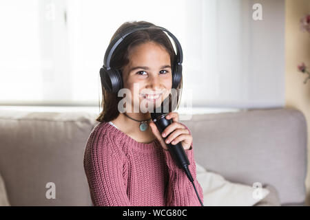 Niña cantando feliz con auriculares y micrófono en interior de la casa Banque D'Images