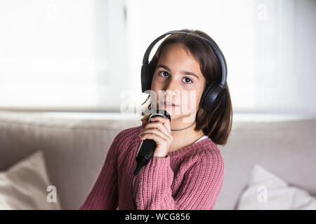 Niña cantando feliz con auriculares y micrófono en interior de la casa Banque D'Images