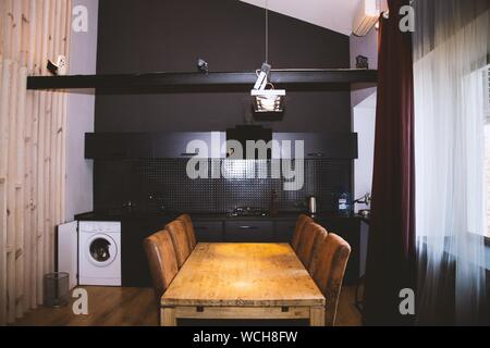 Plan large d'un lave-linge et table en bois avec chaises en bois dans une cuisine avec intérieur noir Banque D'Images