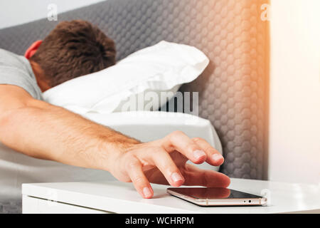 La main de l'homme a essayé de tendre la main en sonnerie de téléphone portable ou d'avoir une certaine alarme répét tôt le matin. Photo aux teintes chaleureuses Banque D'Images